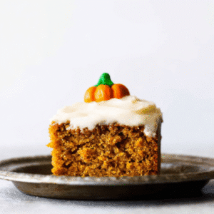 Irresistible Pumpkin Spice Cake Recipe 1 Close-up of a single slice of moist pumpkin spice cake with creamy frosting and a festive candy pumpkin decoration.