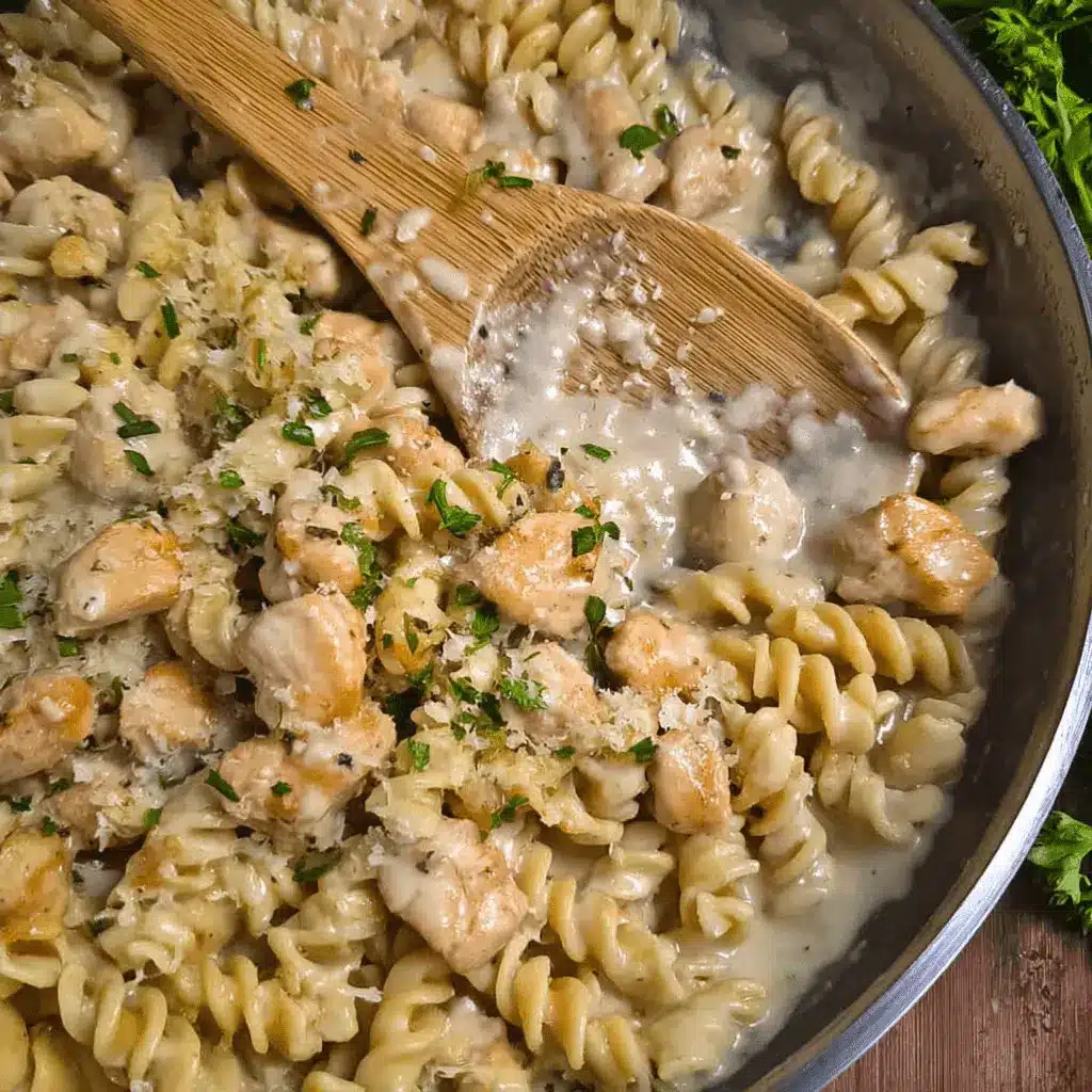 Creamy Garlic Parmesan Chicken Pasta 1 Close-up overhead view of Creamy Garlic Parmesan Chicken Pasta in a metal pan with a wooden spoon, garnished with fresh herbs and Parmesan.