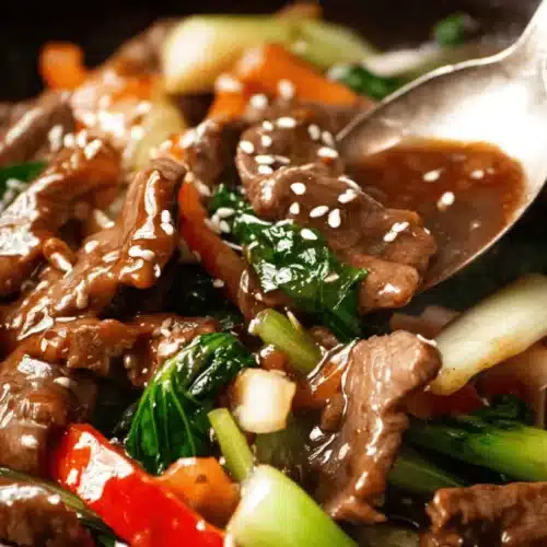 Vibrant beef stir fry with rice, featuring tender beef, crisp bok choy, and red peppers in a glossy sauce, being served.