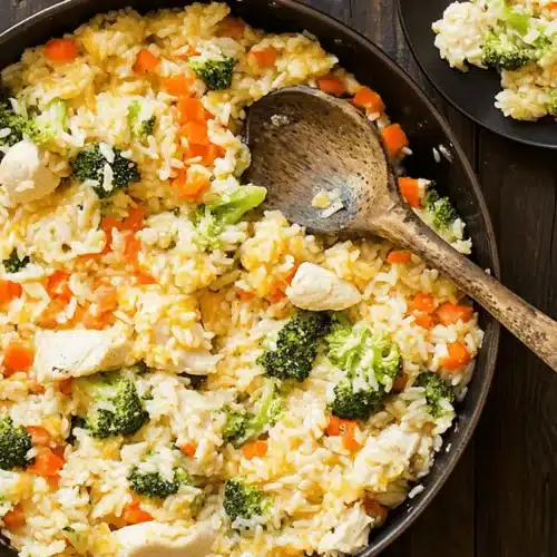 Cheesy One-Pan Chicken Broccoli Rice Skillet 1 A hearty Chicken Broccoli Rice Skillet served in a rustic pan on a dark wooden table with a wooden spoon.