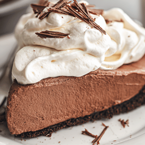 Chocolate Cream Pie Recipe 1 A beautifully presented slice of chocolate cream pie recipe topped with whipped cream and chocolate shavings on a white plate.