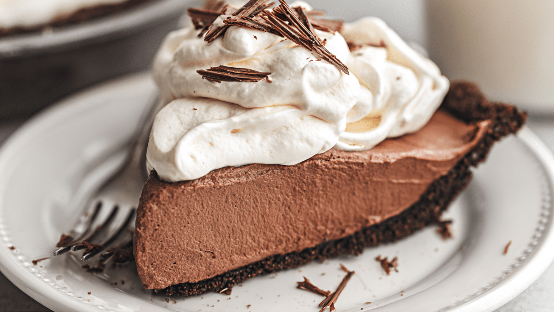 A beautifully presented slice of chocolate cream pie recipe topped with whipped cream and chocolate shavings on a white plate.