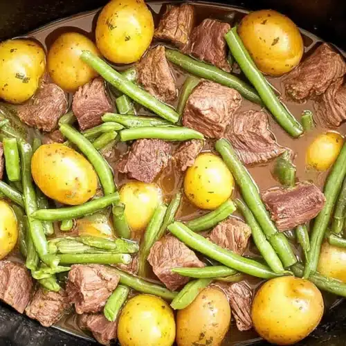 Slow Cooker Garlic Butter Beef Bites with Potatoes 1 Close-up of tender Slow Cooker Garlic Butter Beef Bites with Potatoes and green beans in a slow cooker insert.