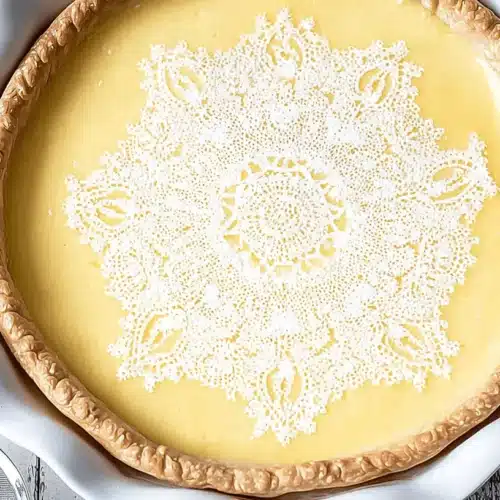 Lemon Custard Pie with Tangy Whipped Cream Recipe 1 Overhead view of a beautifully decorated lemon custard pie with an intricate powdered sugar lace pattern and golden crust.