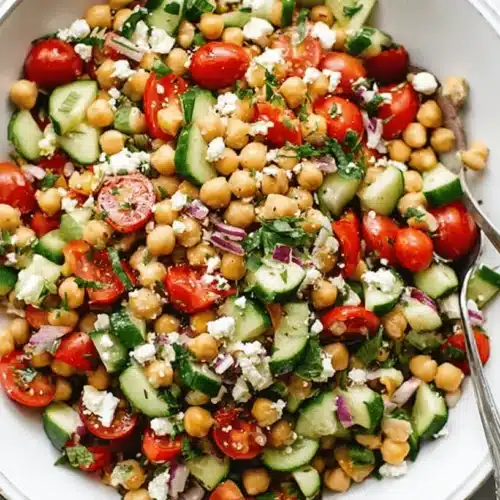 Vibrant Mediterranean chickpea salad in a white bowl with fresh vegetables, feta, and olive oil on a stone countertop.