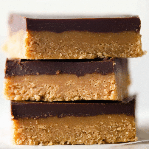 Stack of three delicious no-bake chocolate peanut butter bars with a golden base and rich dark chocolate topping on a light background.