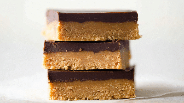 Stack of three delicious no-bake chocolate peanut butter bars with a golden base and rich dark chocolate topping on a light background.