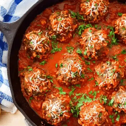 Delicious cast iron skillet of porcupine meatballs in rich tomato sauce, garnished with Parmesan and fresh parsley on a rustic wooden table.