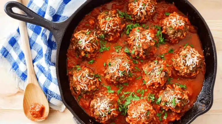 Delicious cast iron skillet of porcupine meatballs in rich tomato sauce, garnished with Parmesan and fresh parsley on a rustic wooden table.