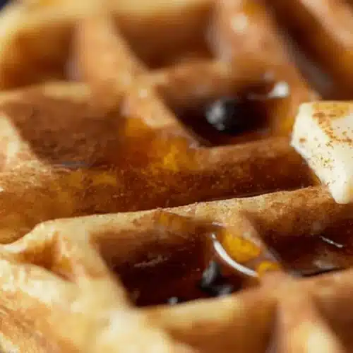 Golden-brown protein waffle with melting butter, maple syrup, cinnamon, and chocolate chips, showcasing a mouth-watering protein waffle recipe.