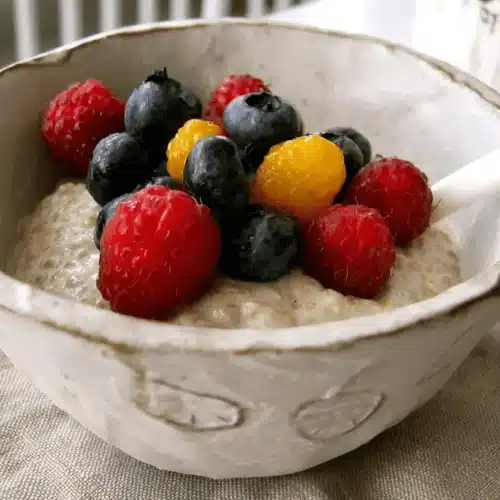 Healthy vanilla chia pudding with berries in a rustic ceramic bowl, topped with fresh raspberries, blueberries, and golden berries, served as a creamy breakfast.